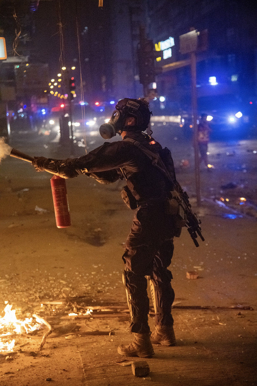 A police officer carrying a rifle uses a fire extinguisher to put out a small - photo 13