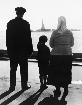 An immigrant family looks at the Statue of Liberty as they await the barge that - photo 3