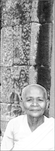 A Buddhist nun sits next to the lacework reliefs of the Bayon temple at Angkor - photo 2