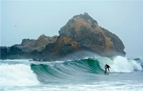 A surfer rides the waves at Pfeiffer Big Sur Beach decorated with sea stacks - photo 9