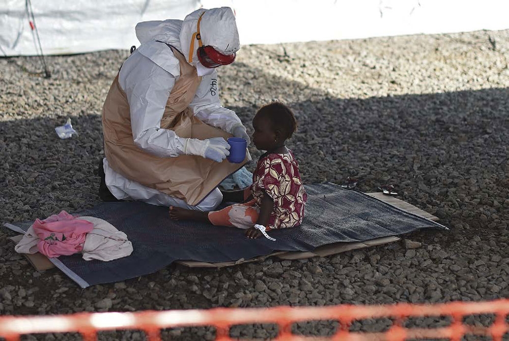 A health worker wears protective equipment while offering a drink to a young - photo 4