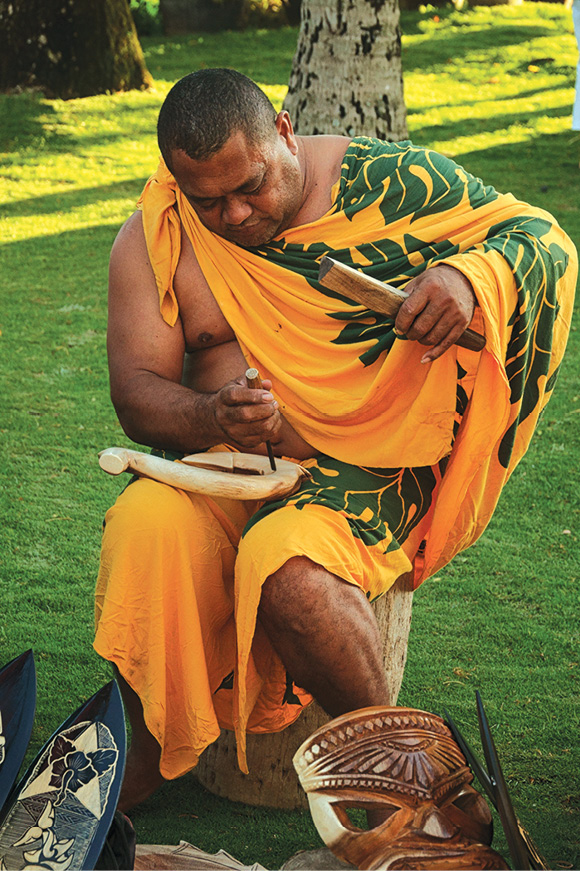 An artisan in traditional Polynesian garb handcarves wooden keepsakes at the - photo 23