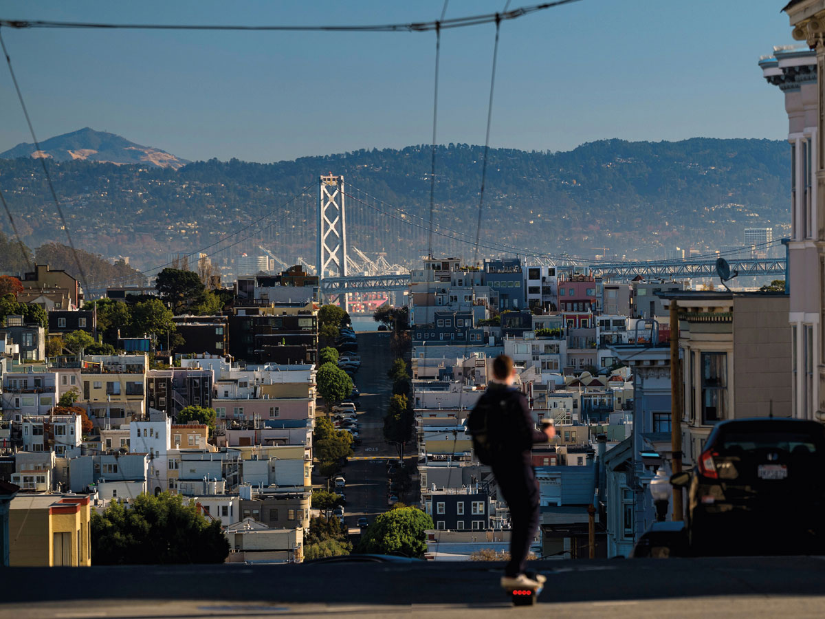 A young man on an electric skateboard heads towards the Bay Bridge which links - photo 7